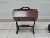 Front view of the vintage wooden sewing basket on wooden stand, showing closed lids and handle on top.
