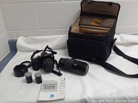 View of camera, lenses, film canisters, manual and carrying case