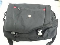 Front angled view of black Swissgear messenger bag with flap partially open showing clasp and zipper pocket