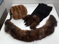 Overview of mink muff, fox collar, and black scarf with fox fur accents laid out on white surface.