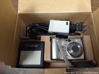 Open box showing Nikon Coolpix 5900 camera, black battery charger, and power cable.