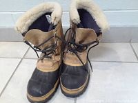 Front angle view showing the lace-up design, black rubber toe caps and soles, and the boots' color contrast between tan upper and black lower part.