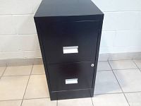 Full view of the black metal 2 drawer filing cabinet showing lock and handles, standing on tile floor against white wall.