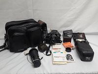 Full lot showing Konica PF-1 camera, leather carrying bag, Vivitar flash, lens hood, battery, manuals, and accessories arranged on table.