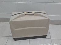 Singer portable sewing machine stored in beige hard plastic carrying case with handle.
