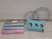 Photo of two metal wreath frames, three rolls of craft mesh in blue, gray, and pink, and one turquoise bear-themed decorative cushion.