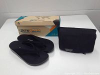 Full view of Aerothotic brand flip-flop sandals with original shoe box and black fanny pack.