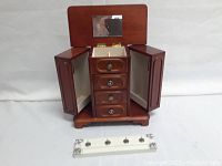 Wooden jewelry box open to show mirror, three drawers in center, and two side compartments.