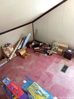 Photo of attic corner with various items including wrapping paper, boxes, board games and small collectibles displayed on pink carpet under slanted ceiling.