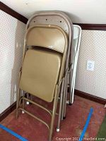 Four folding chairs stacked together against the wall showing metal frames and different colors including beige, gray, and white.