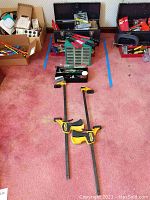 Wide shot showing two Craftsman toolboxes filled with various hand tools, a organizer with small drawers, and several bar clamps laid out on carpet.