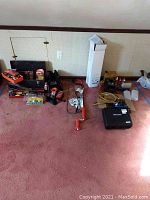 Full overview of lot laid out on pink carpet showing tool box, hand tools, inspection camera case, rope, and boxed items.