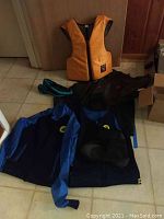Wetsuit jacket, wetsuit pants, boots, life preserver, raincoat, hat and aqua shoes arranged on floor