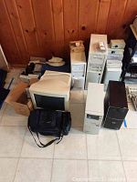 Group photo showing five desktop computer towers, two CRT monitors, and a black carrying bag on floor against wood-paneled wall.