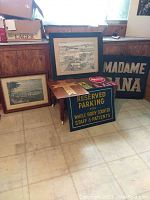 Framed sketches, multiple metal signs, and wood cross grouped on floor and small table