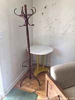Full view of wooden coat rack standing next to yellow retro style table with white top in a corner next to a beige couch
