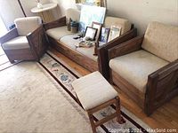 Two beige cushioned wood framed chairs and one beige cushioned wood framed ottoman in a room, shown from front angle
