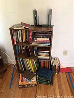 Full view of wooden bookcase with books, magazines, and some stacked on floor