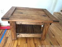 Solid wood end table with thick legs and a lower shelf, wood grain visible, square shape.