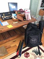 Overview of the bag contents on a table and floor showing musical instruments and accessories, including harmonicas, maracas, guitar strings and a Klos guitar bag.