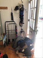 Wide view of corner showing two black foldable shopping carts, several hats stacked vertically on a holder, jackets or sweatshirts piled in a box, and an umbrella hanging on the wall next to a door.