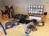Full view of kitchen counter with cutting block, knife sharpeners, metal tray with flatware, spice rack, paper towel holder, and assorted items