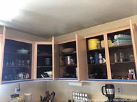 Photo of open kitchen cabinets revealing vintage plastic storage containers, glassware, crocks, and other kitchen items