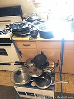 Multiple Calphalon pots and pans piled on stove and floor showing variety of sizes