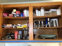 Kitchen cabinet upper shelves showing various items including kitchenware, cookbooks, paper cups, a pewter mug, and canisters.