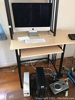 Wide view of iMac on desk with keyboard and trackpad on top shelf, UPS units, speaker subwoofer and cords underneath