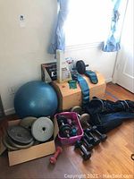 Wide shot showing the collection of workout items near a window, including weights, blue exercise ball, and bags.