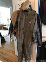 Group shot showing brown shearling flight jacket, olive drab flight suit and black leather jacket on hooks.