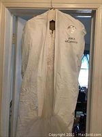 Jessica McClintock garment bag with the wedding dress inside, hanging on a door.