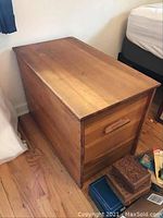 View of rectangular cedar chest showing top surface and one long side with natural wood grain and visible scratches and stains.