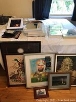 Multiple framed artworks, picture frames, and a table mirror on bed and floor