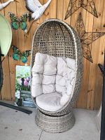 Egg-shaped aluminum wicker swivel chair with beige tufted cushion against wood wall