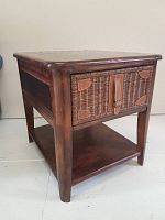 Front three-quarter angle view of the dark wood side table with rattan drawer and lower shelf