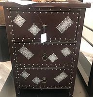 Front view showing the brown leather surface with metal studded diamond patterns and metal ring handles on lower drawers.