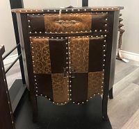 Front view of the two-tone decorative chest showing intricate design panels, nailhead trim, metal hardware, and curved legs.
