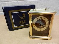 Front view of the vintage JAZ Paris quartz mantle clock with original box behind it, showing clock face with Roman numerals and gold-tone frame.