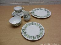 Wedgwood tea set items arranged on table showing cup, saucer, creamer, bowl, small plate, and large plate with green ivy leaf pattern.