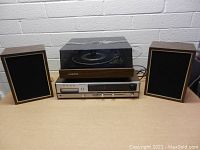 Front view of the entire stereo setup showing the turntable with dust cover on top of the amplifier and the two speakers on either side.