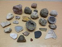 Top-down view of 25 assorted rocks, geodes, and fossils laid out on a table showing a variety of colors, textures, and sizes.