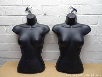 Front view of two black female torso hanging forms on hooks, showing bust, shoulders, and waist.