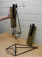 Photo showing one candle holder mounted on the wooden backplate, held by hand for scale, with the other backplate and holder on the table.
