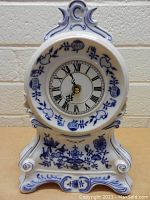 Front view of white porcelain mantel clock with blue onion pattern and Roman numeral face