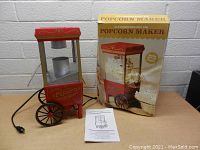 Nostalgia hot air popcorn maker in the style of a vintage popcorn cart with original box and instruction manual, front view.