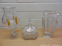 Three crystal items on table: vase with amber accents, covered square dish, and clear crystal lamp base