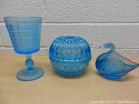 Side view of the lot showing the goblet, covered bowl, and swan figurine made of vintage blue glass