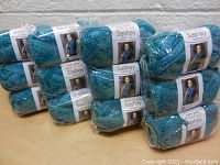12 skeins of Red Heart Sashay yarn in metallic blue color arranged on a table, still in original plastic packaging with visible labels.